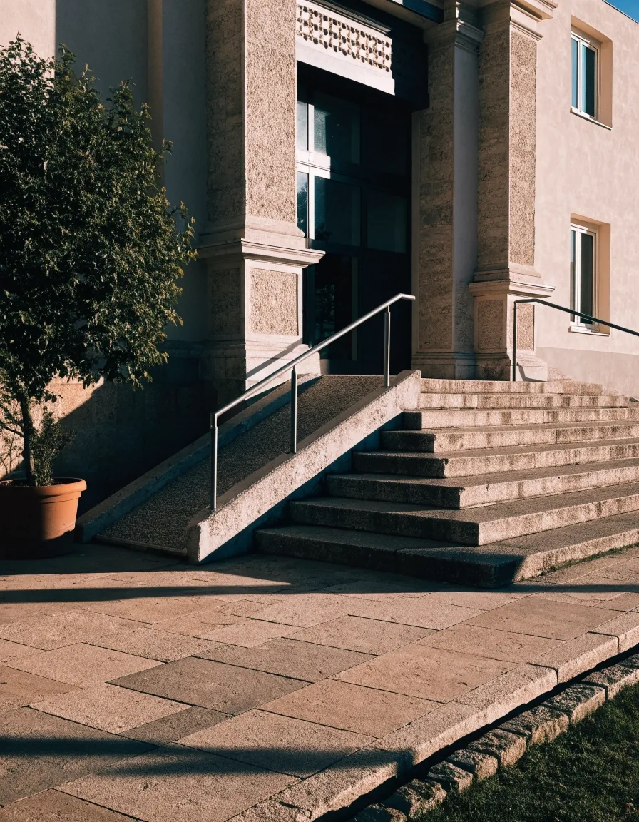 Entrada de un centro cívico español con rampa accesible y barandilla metálica a última hora de la tarde